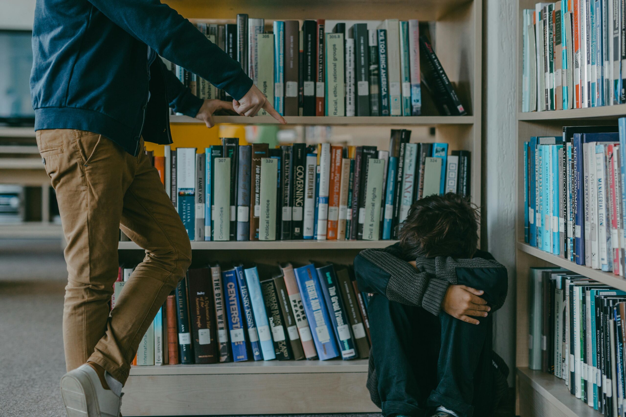 A child facing bullying while sitting in a library against bookshelves, depicting harassment and isolation.